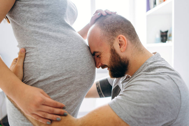 Pregnancy. Young couple waiting for baby. Wonderful expectant parents cuddle in their apartment awaiting birth - Foto, Bild