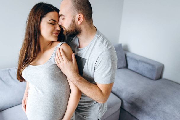 Pregnancy. Young couple waiting for baby. Wonderful expectant parents cuddle in their apartment awaiting birth - Zdjęcie, obraz