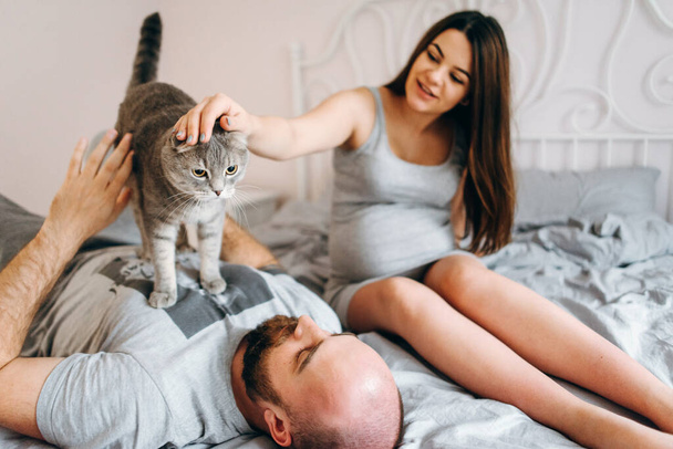  Junges Paar wartet auf Baby. Schwangere Frau und Mann mit Katze im Bett - Foto, Bild