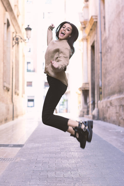 Moderní a usmívající se mladá dívka skákání šťastně na jasné ulici - Fotografie, Obrázek