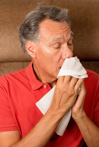 Mann mit Grippe niest in seinem Haus in ein Taschentuch - Foto, Bild