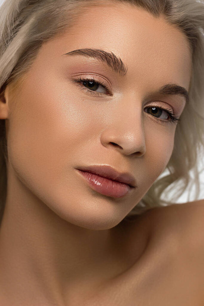 Closeup portrait of a woman with developing curly hair. Sweet tender young blonde girl. Natural lipstick, clear clear skin. Skin care with natural cosmetics in a spa or cosmetology. - Valokuva, kuva