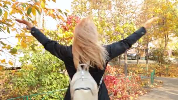 Onnellinen aikuinen pitkätukkainen blondi nainen trenssitakissa reppu pyörii avosylin puistossa. Ulkona. Iäkkäät ihmiset ja viestinnän käsite
. - Materiaali, video