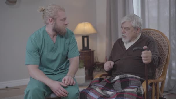 Portrait of Caucasian man listening to stories of upset retiree in nursing home and holding his hand. Male nurse supporting old man. Care, help, volunteering, lifestyle. - Materiał filmowy, wideo