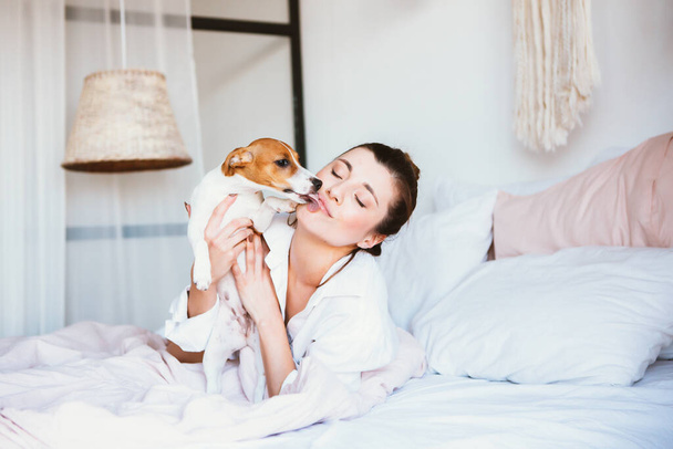 Woman and dog play on the bed. - Foto, Bild