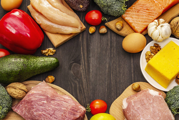 Trendy ketogene dieetproducten set. Paleo, pegan lage koolhydraten voeding. Vlees, vis, kaas, fruit en groenten. Zwarte houten planken achtergrond - Foto, afbeelding