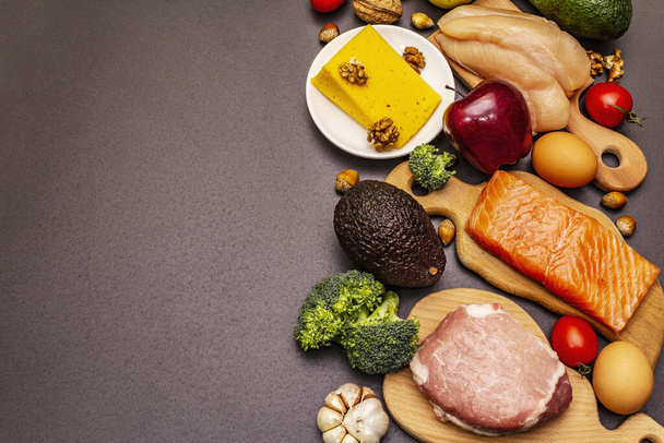 Trendy ketogene dieetproducten set. Paleo, pegan lage koolhydraten voeding. Vlees, vis, kaas, fruit en groenten. Zwarte steen betonnen achtergrond - Foto, afbeelding