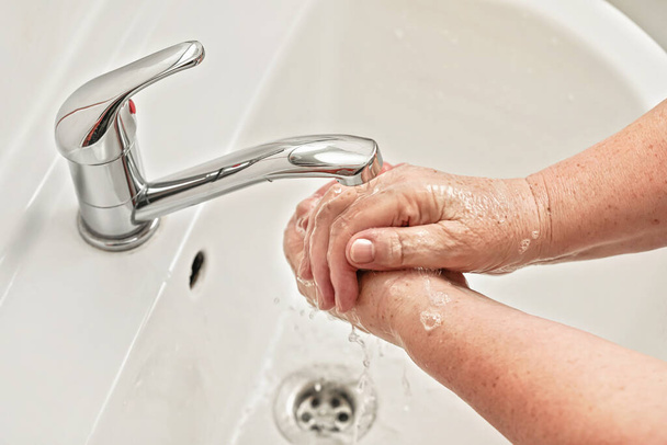Donna anziana si lava le mani con il sapone sotto il rubinetto dell'acqua del rubinetto. Può essere utilizzato come concetto di illustrazione igiene durante ncov coronavirus / covid 19 focolaio
 - Foto, immagini