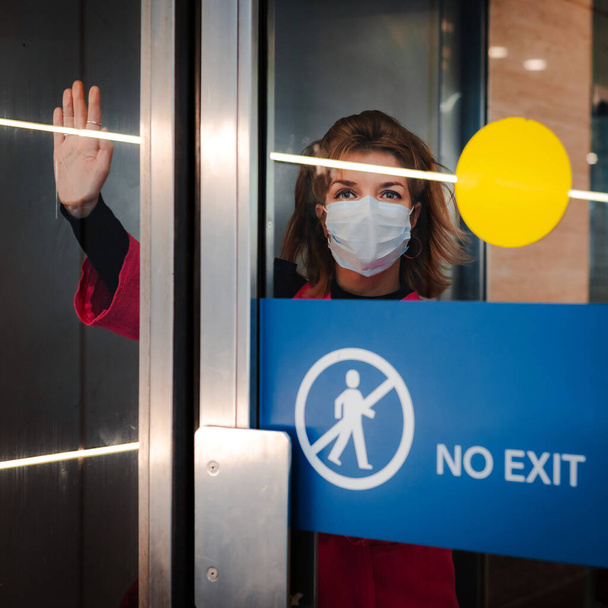 Stop infectie. vrouw toont stop gebaar door glazen deur er is geen uitgang. meisje draagt een beschermend masker tegen infectieziekten griep in een openbare plaats. Het begrip gezondheid, de quarantaine. - Foto, afbeelding
