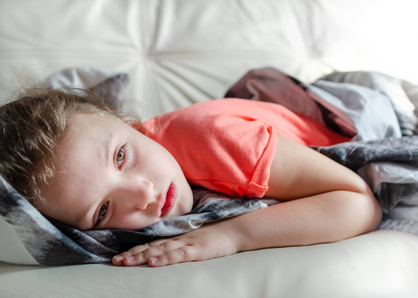 Sick girl lying on the sofa at home. Sad mood, kid alone and quarantine concept. - Photo, Image