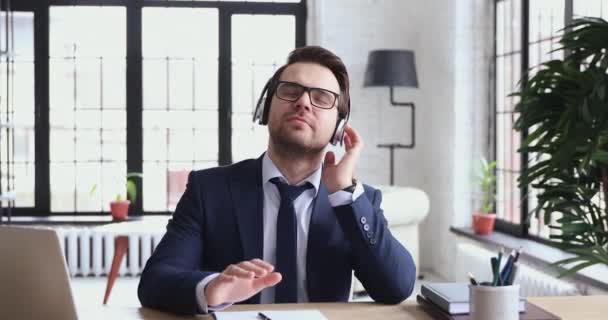 Relaxed funny male executive listening to music wearing wireless headphones - 映像、動画