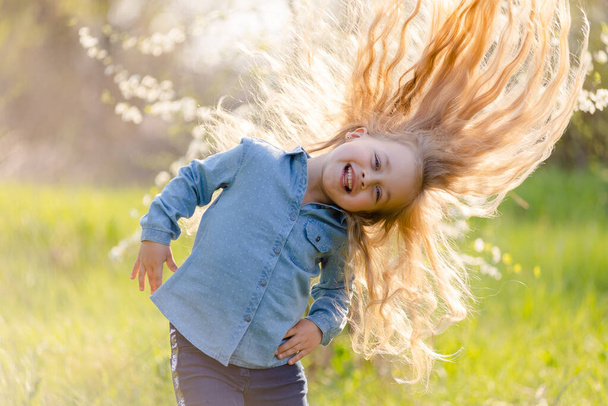 Petite fille avec de beaux cheveux épais s'amuse dans le parc de printemps
. - Photo, image