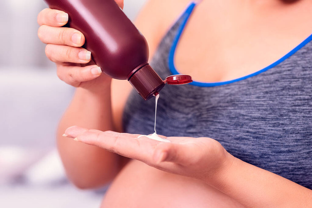 Femme enceinte appliquant une lotion corporelle sur la main
. - Photo, image