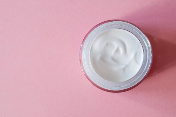An open glass jar with white cream for the face or body on a pink background. Skincare concept. Horizontal orientation. Copy Space. Top view. - Fotoğraf, Görsel