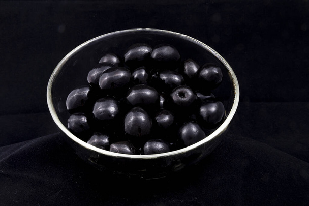 чорні оливки в скляній мисці на чорному фоні
 - Фото, зображення