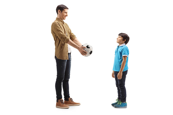 Full length shot of a young man giving a soccer ball to a boy isolated on white background - Foto, Bild