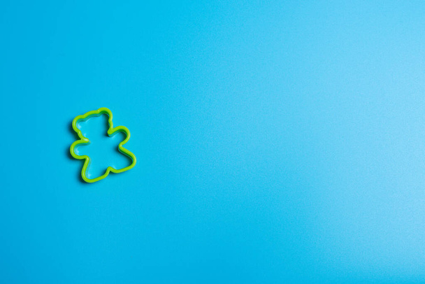 Green plastic cookie cutter for making cookies in the shape of a teddy bear on a blue background. Culinary concept. Flat lay with copyspace. - 写真・画像