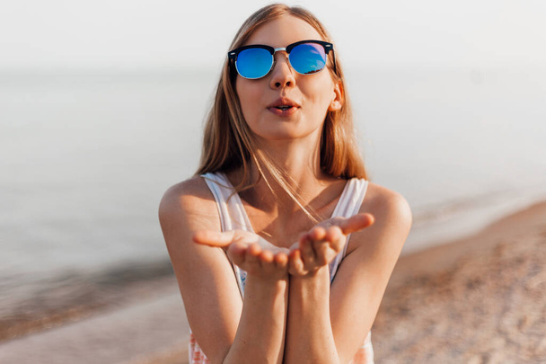 Close up of a cheerful young girl in sunglasses taking a selfie on the beach and sending a kiss - Foto, Bild