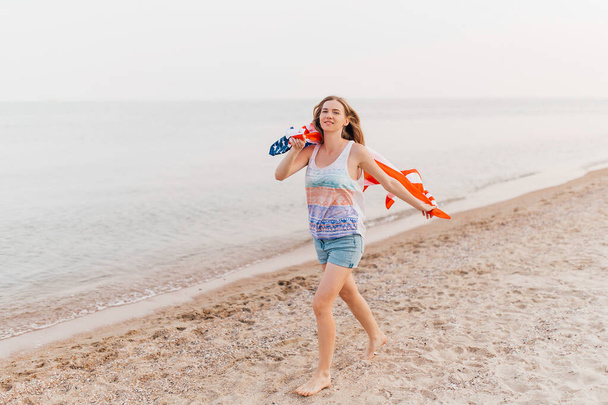 Image of a happy woman outdoors on a beach holding a US flag and having fun - Foto, immagini