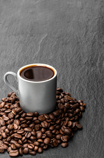 Café noir dans une petite tasse avec des haricots sur fond de pierre noire  - Photo, image