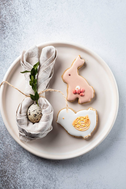 Table setting for the holiday of Easter. The photo shows white dishes, serving mat, Easter egg in a napkin. Napkin draped under rabbit ears. - Foto, Imagen
