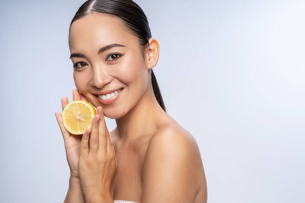 Happy young woman showing a fresh lemon in studio - Photo, Image