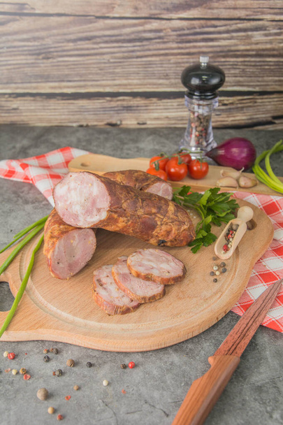 Sausage with minced meat, cut into small pieces on a wooden board with spices and herbs. Side view. - Foto, Bild