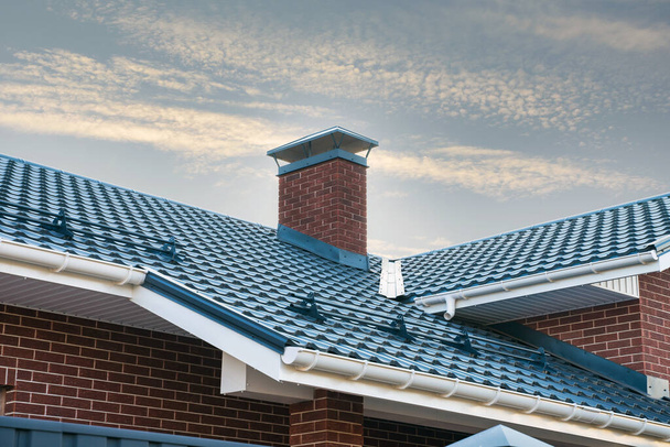 Nieuw geïnstalleerde constructie frame huis regen dakgoot systeem op het metalen dak. Baksteen schoorsteen pijp tegen de blauwe lucht. - Foto, afbeelding