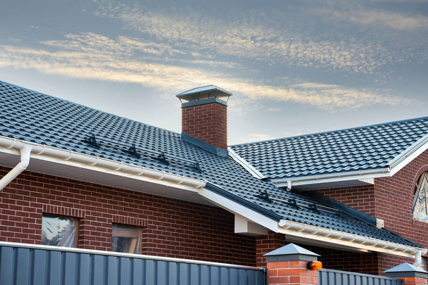 Système de gouttière de pluie nouvellement installé sur le toit en métal. Tuyau de cheminée en brique. Portes métalliques automatiques
. - Photo, image
