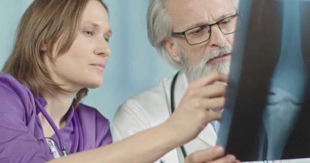 Ανώτερος Γιατρός και νεαρή γυναίκα τεχνικός ιατρικής κοιτάζοντας μια ακτινογραφία του γονάτου - Πλάνα, βίντεο
