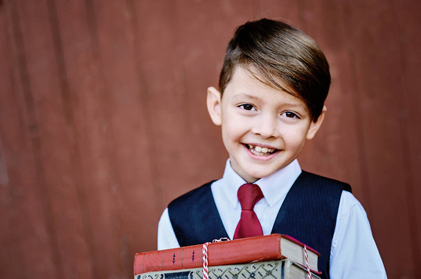 Portrait d'un garçon d'école heureux debout avec des livres sur fond de bois rouge.. Adieu Bell. jour de la connaissance. début de l'année scolaire
. - Photo, image