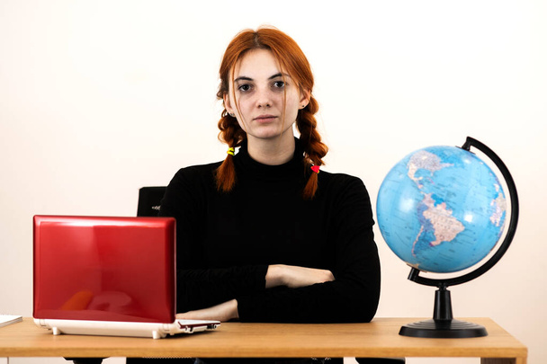 Feliz joven trabajadora de oficina sentada detrás de un escritorio de trabajo con computadora portátil, teléfono celular, portátil y globo geográfico del mundo
. - Foto, Imagen