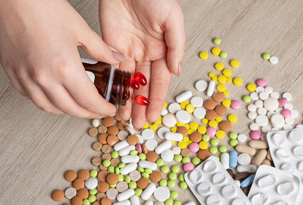 Tabletten in verschiedenen Formen und Farben verstreut auf dem Tisch und in den Händen. Leere Medizin-Blisterverpackungen. Pillen-Hintergrund - Foto, Bild