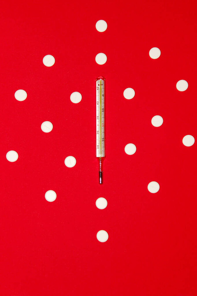 Gesundheit und medizinischer Hintergrund, vertikale Ansicht. Thermometer und weiße Pillen auf rotem Hintergrund. Abstrakter medizinischer Hintergrund. - Foto, Bild