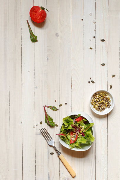 здоровый салат из бобов и конопли и семян тыквы в белой миске с вилкой и тарелкой с проросшим зерном, вид сверху с пространством
 - Фото, изображение