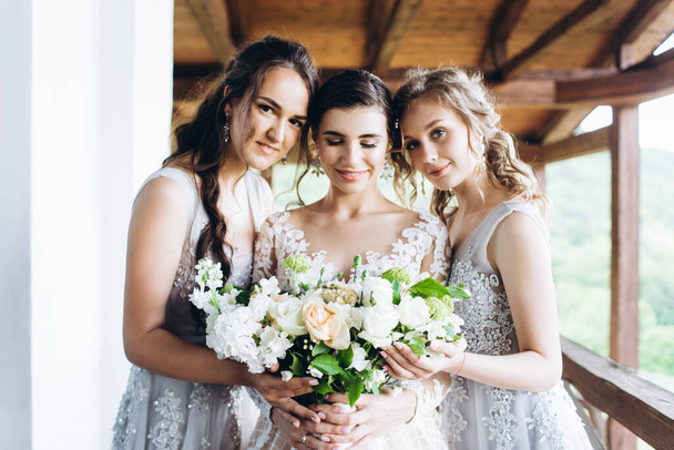 Young bride with friends look at a wedding bouquet on the hotel balcony. - Fotoğraf, Görsel