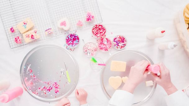 Flat lay. Step by step. Little girl decarting sugar cookies with royal icing and sprinkles for Valentine's Day. - Photo, Image