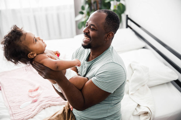Cheerful Afro American man holding cute baby girl in arms - Фото, зображення