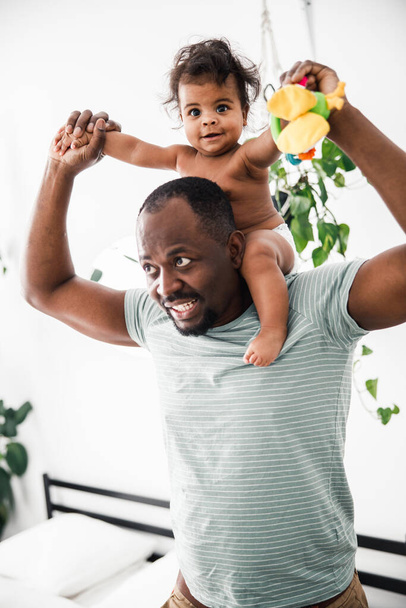 陽気なアフリカ系アメリカ人の男彼の肩に赤ちゃんを運ぶ - 写真・画像