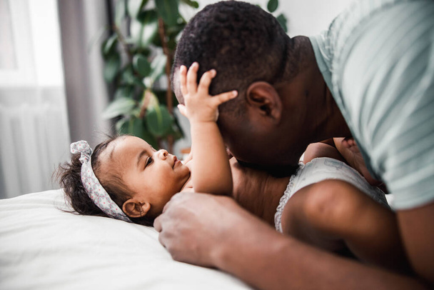 Afro American man kissing belly of cute newborn daughter - 写真・画像