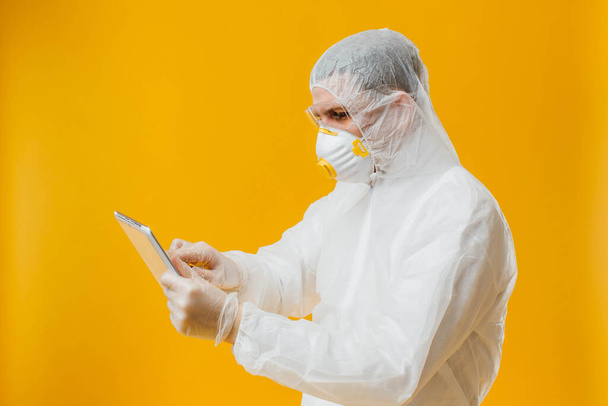 epidemiologist in hazmat suit and respirator mask holding digital tablet on yellow background - Photo, Image