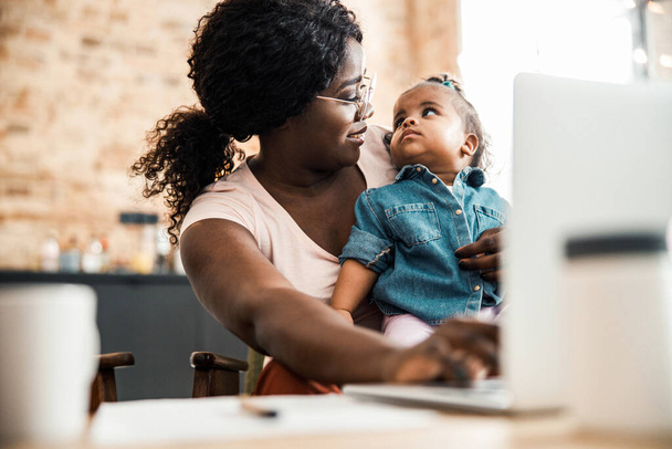 Charming Afro American lady holding baby girl and using laptop - Foto, immagini