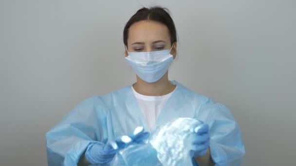 Kobieta lekarz zakłada czapkę medyczną przed zabiegiem chirurgicznym w klinice. Portret kobiety w mundurze medycznym, maska ochronna i rękawiczki lateksowe. Kosmetyk przygotowujący się do pracy - Materiał filmowy, wideo