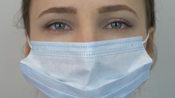Woman's face in protective medical blue mask, close up. Young female wearing medical mask for virus infection prevention and protection. Pandemic protection of the Covid-19 coronavirus. - Кадры, видео