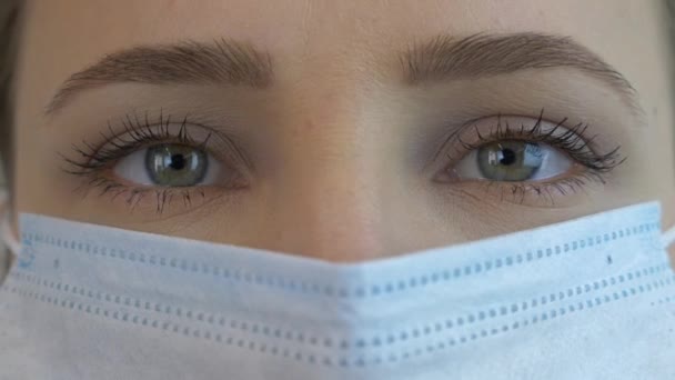 Female face in medical face mask for virus infection prevention and protection, extreme close up. Pandemic protection of the Covid-19 coronavirus. Woman with green eyes in protective medical mask - Кадры, видео