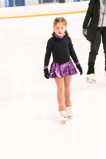 Mała dziewczynka ćwiczy łyżwiarstwo figurowe na krytym lodowisku. - Zdjęcie, obraz