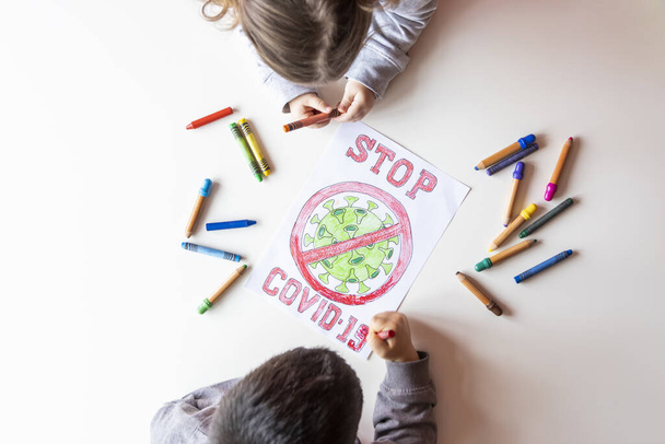 Onherkenbare jongen en meisje kleur een tekening van stop coronavirus op een witte tafel, bovenaanzicht - Foto, afbeelding
