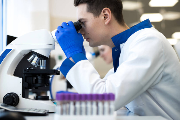 Male researcher in sterile gloves using laboratory microscope - Fotó, kép