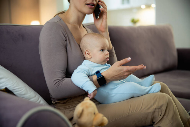 Smiling young mom sitting with baby and using smartphone - Foto, immagini