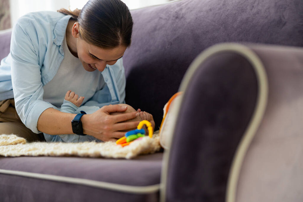 Hymyilevä nainen ja söpö lapsi leikkii sohvalla olohuoneessa
 - Valokuva, kuva